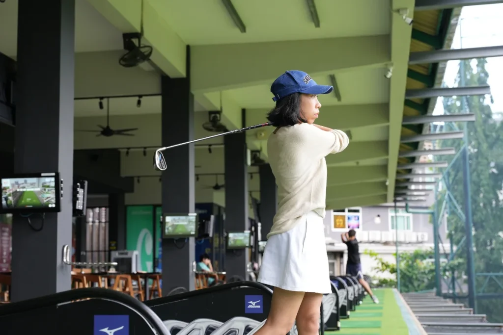 Female golfer training inside a covered driving range at Bangkok Bay with launch monitor feedback.