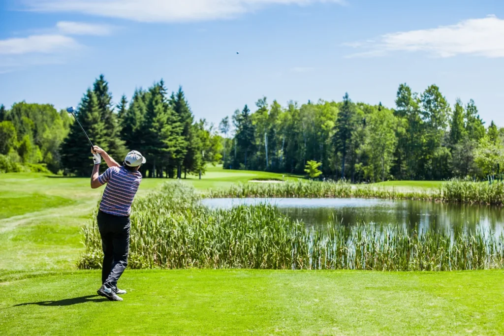 Male golfer hitting a drive outdoors, showing full ball flight in real course conditions.